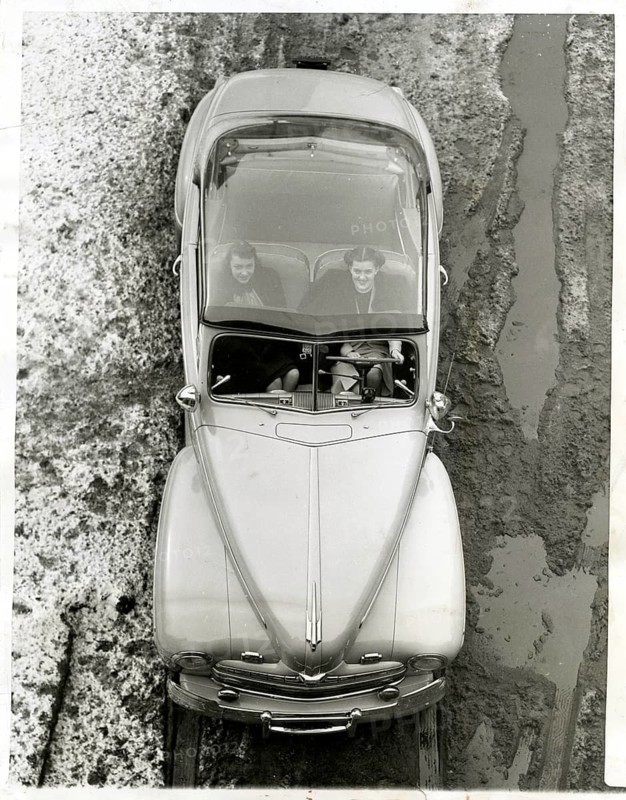 USA, vintage car, Ford, transparent car roof, woman, winter, A bird's-eye view car on a wet road driving through puddles of water, in the style of the 1950s