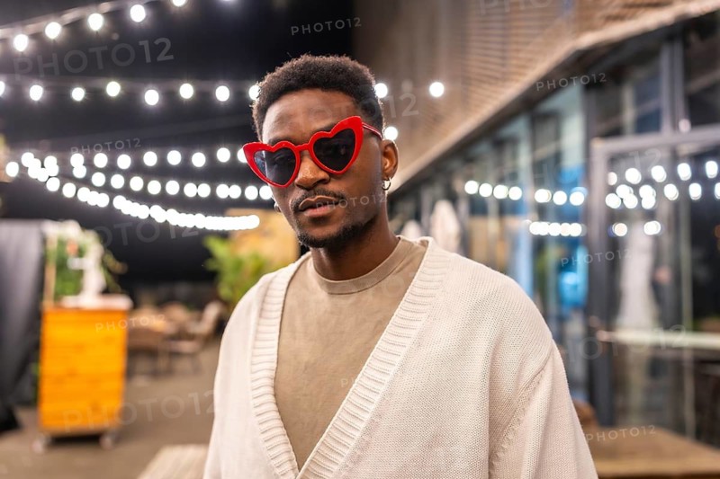 Portrait of a modern cool african man with heart shaped sunglasses standing in a bar terrace at night