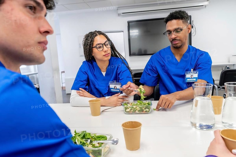Healthcare professionals in blue scrubs enjoying a healthy salad meal and water during a team lunch break, fostering camaraderie and discussion in a medical environment