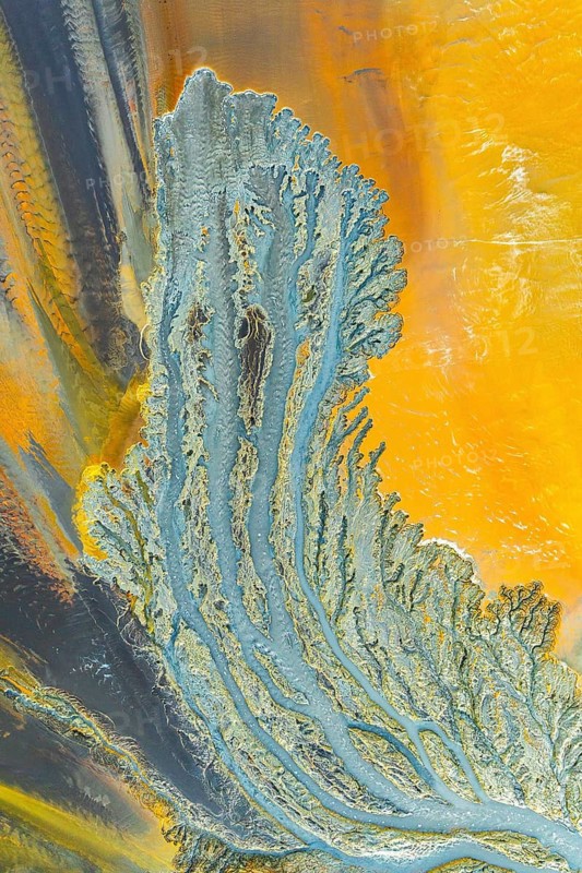 A stunning aerial view showcasing intricate fractal patterns in mud, blending vibrant yellow and blue hues. The natural design highlights organic shapes and textures