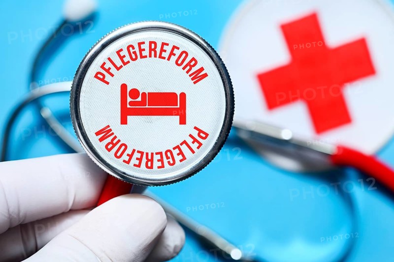 Hand holding stethoscope with inscription care reform and pictogram of a hospital bed, photo montage +++ editorial use only