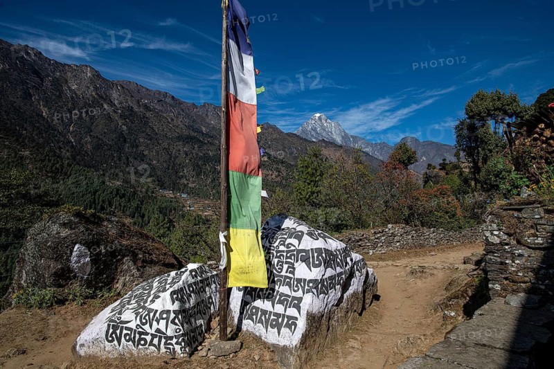 Buddhist prayer flag and holy mantras on manistones in front of mountain landscape on the way to Mount Everest, Solu Khumbu, Himalayas, Nepal