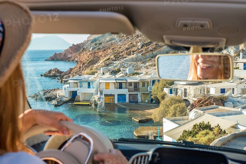 A driver enjoys a scenic view of the charming coastal village of Fourkovouni on Milos Island, Greece, showcasing whitewashed houses by the turquoise Aegean Sea