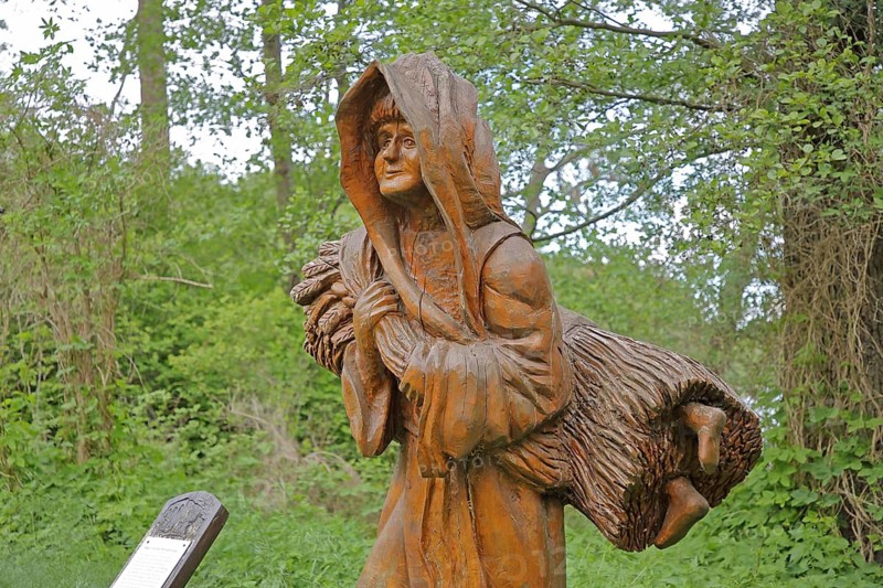 Wooden sculpture of legend on the straw bridge, monk secretly smuggles child in sheaf into the monastery, shoes made of straw peeking out, hidden, modern art, wood carving, life-size, Himmelpfort, Fürstenberg-Havel, Uckermark, Brandenburg, Germany