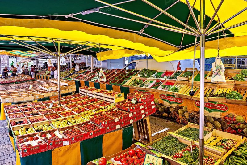 A colorful market stand with fruit and vegetables under large yellow and green umbrellas, market stalls in Brittany