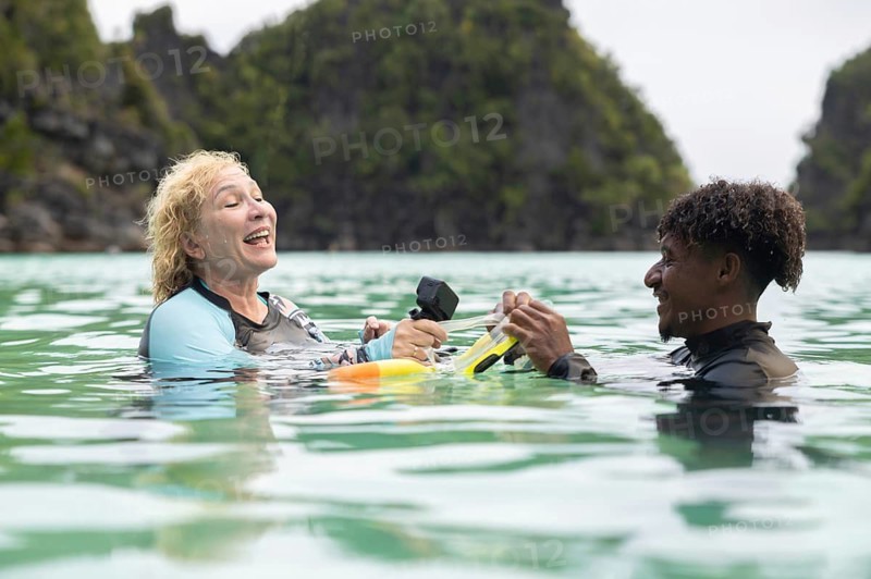 Tourist and guide enjoy snorkeling in the crystal-clear waters of Raja Ampat, West Papua, surrounded by lush green cliffs They share a moment of joy and a deep appreciation for nature