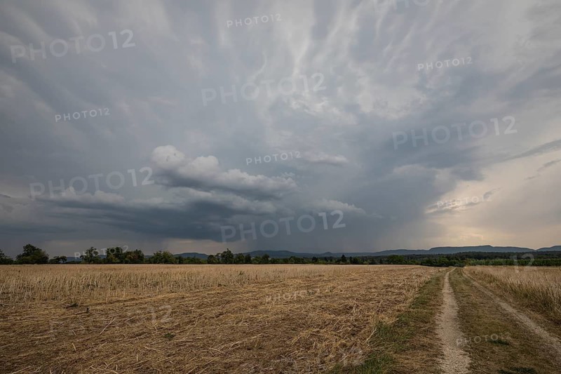 Dramatic dark storm clouds gather over a harvested stubble field with a dirt path leading toward the Swabian Alb in Germany