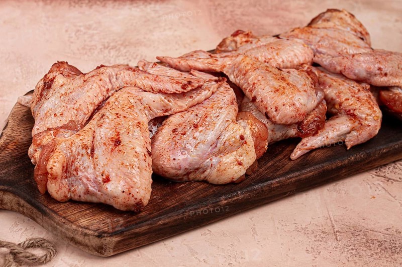 Chicken wings, marinated and laid out on a wooden platter, ready for cooking, grilling or baking, in a home kitchen, there are no people