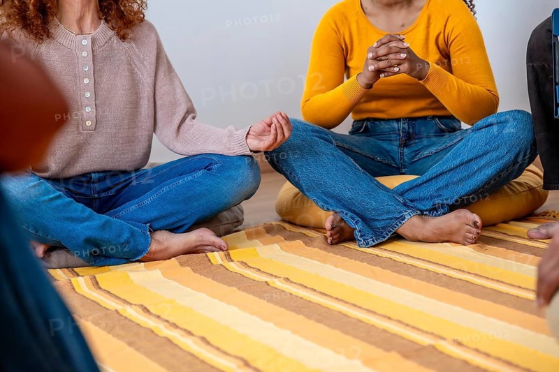 Diverse women gathering for group meditation, practicing mindfulness and sharing support while seated on floor cushions, fostering wellness and mental health
