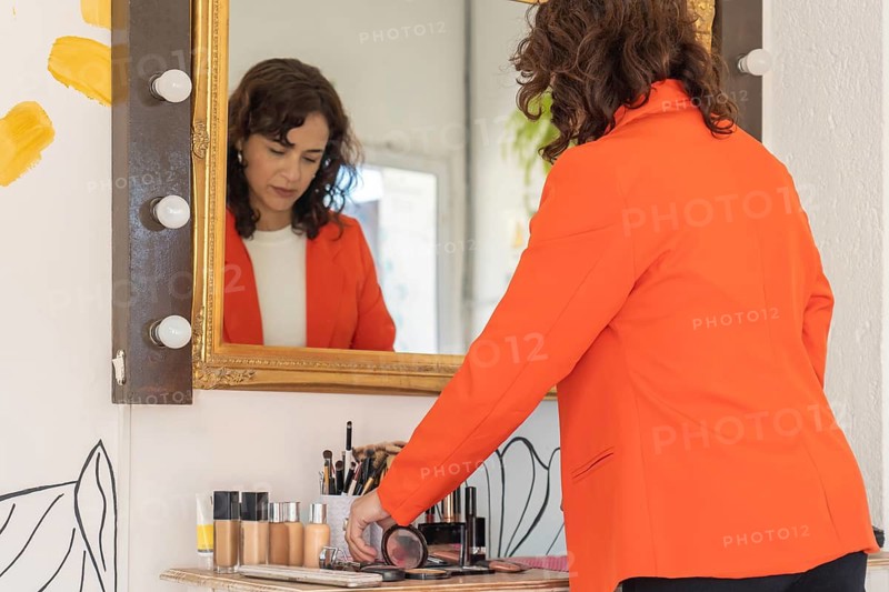 Rear view of a makeup artist arranging cosmetic products and beauty tools in front of a salon vanity mirror