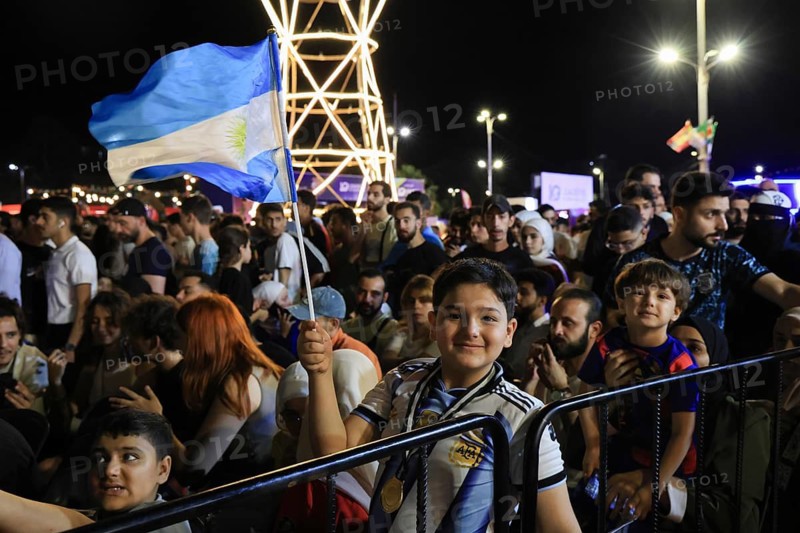Damascus, Syria - July 19, 2026: A young boy waves the Argentine national flag high amidst thousands of fans gathered at a public viewing area to watch Argentina and Spain compete in the 2026 FIFA World Cup final match broadcast on giant screens, Damascus, Damascus, Syria