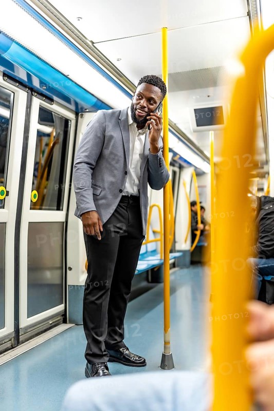 Young businessman engaging in a phone conversation while commuting on a subway train, confidently navigating the urban transport scene