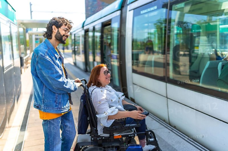 Young man assisting disabled woman in a wheelchair as they board a modern tram in the vibrant city, promoting accessibility and kindness