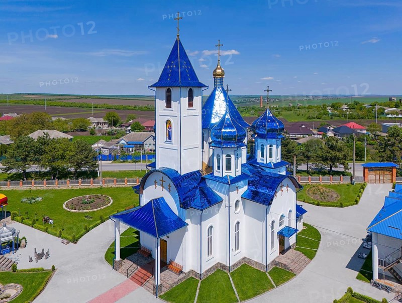 Church with blue roofs and white façade, nestled in a rural setting under a blue sky, aerial view, Church of the Protection of Our Lady, Biserica Acoperamântul Maicii Domnului, Tarigrad, Drochia District, Republic of Moldova, Moldova