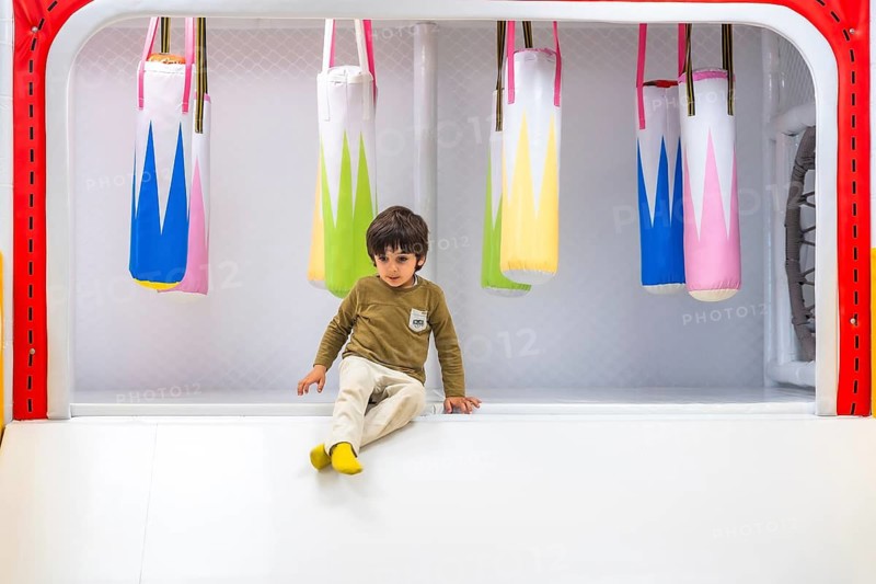Young child sitting near colorful hanging punching bags in a safe, padded indoor play area designed for toddlers