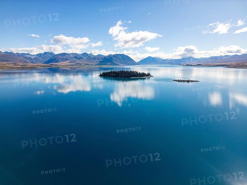 Aerial view of Lake Tekapo in Canterbury, New Zealand, showcasing a breathtaking turquoise lake with a small forested island, surrounded by a mountainous landscape