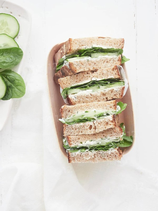 Healthy vegetable sandwiches with cucumber and green spinach leaves, placed cut in halves in recyclable basket tray