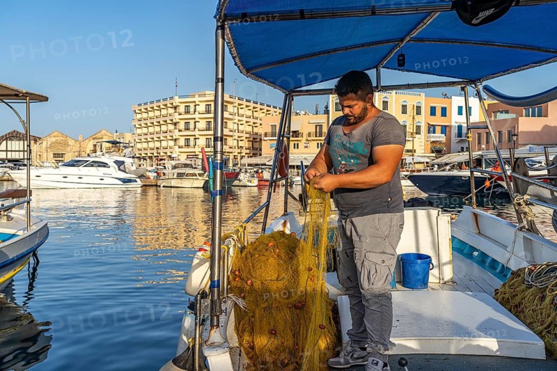 Fisherman with his net on a boat in the harbour of Chania, Crete, Greece