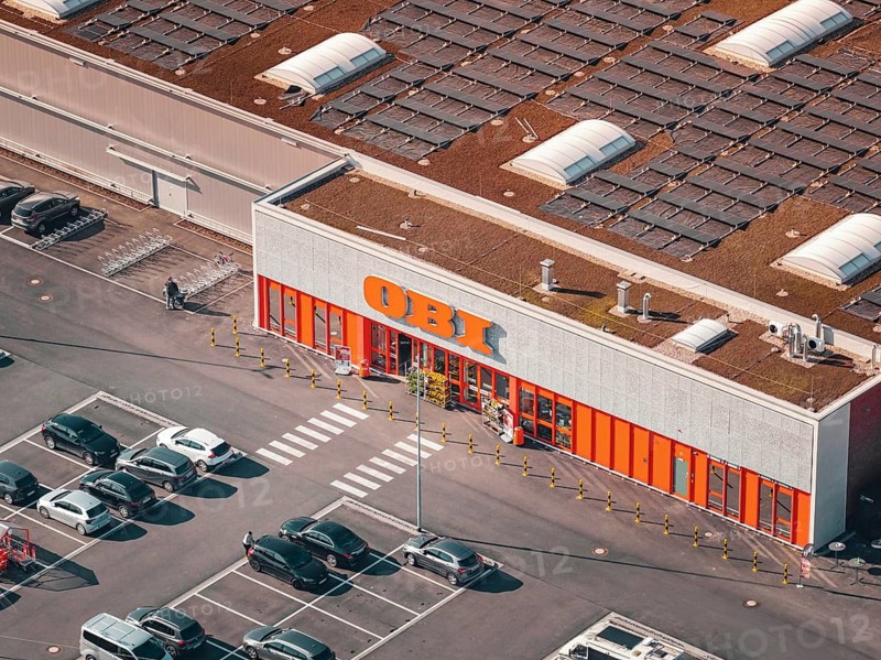 Building with visible brand logo and solar panels on the roof, surrounded by parking spaces, PV Bau Auf OBI Bau Markt, Mühlacker, Enzkreis, Germany