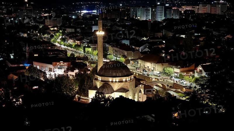 Nighttime cityscape with illuminated mosque and surrounding buildings illuminating the night sky, Prizren, Kosovo