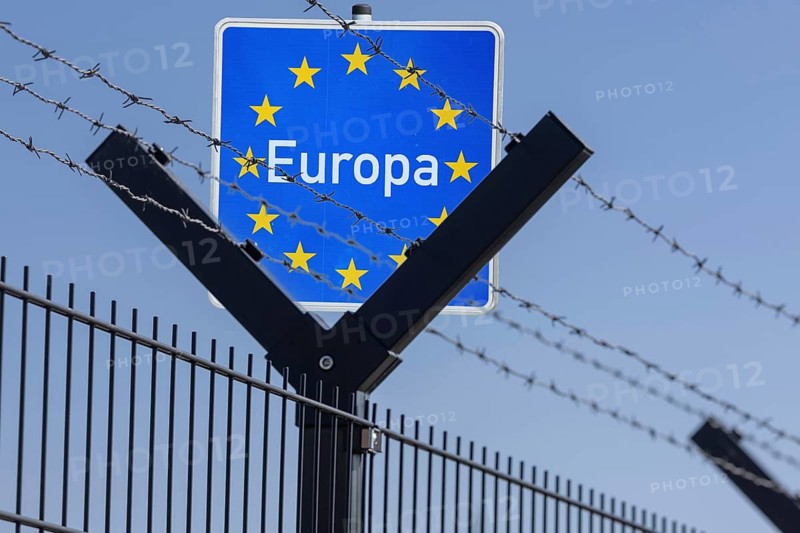 (photo montage) Symbolic image: border sign with the inscription EUROPE behind security fence with barbed wire