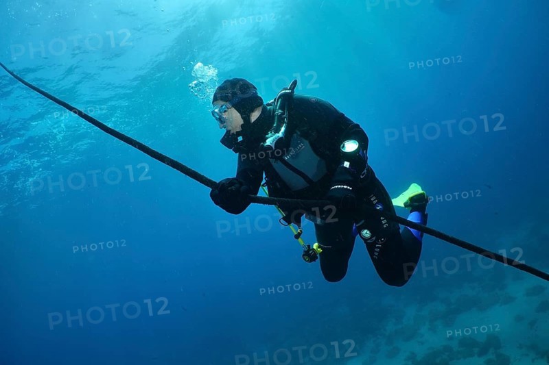 Diver holding on to a rope, floating in the blue underwater. Slow descent along the anchor line. Dive site Punta Negra, Las Galletas, Tenerife, Canary Islands, Spain