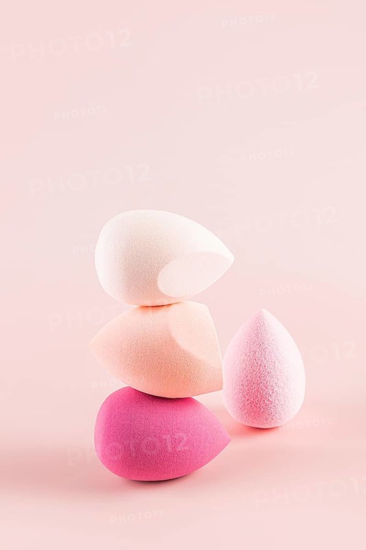 Delicately balanced stack of vibrant makeup sponges, showcasing various shapes and shades of pink and white, set against a soothing pink backdrop