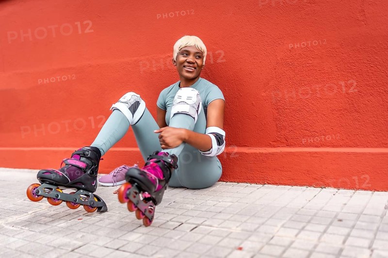 Tired african urban sportive woman sitting on the street wearing inline skates