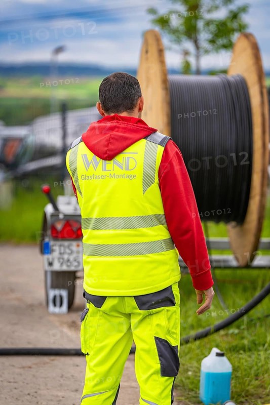 A construction worker in safety clothing works near a large cable drum on a road, fibre optic installation, Calw district, Black Forest, Germany