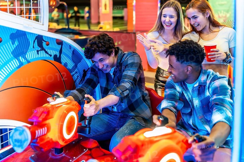 Happy multi ethnic friends playing arcade basketball game in an amusement park, having fun together