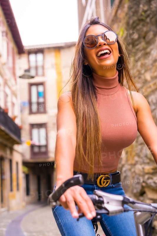 Pretty latin woman with sunglasses doing bicycle sightseeing in the city through the old town. Eco tourism in summer on vacation, model riding the bike smiling