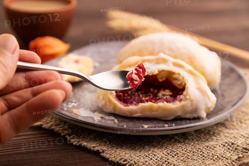 Glazed Pies with Cowberry jam on brown wooden background and linen textile with hand, cup of coffee, side view, close up, selective focus