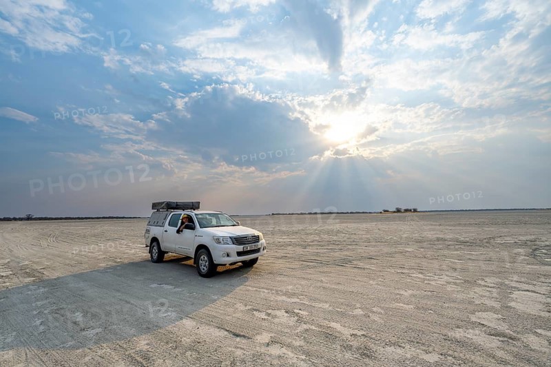 Young man looking out the window of an off-road vehicle, Toyota Hilux on a salt pan, dramatic clouds with sun rays, Nxai Pan National Park, Botswana