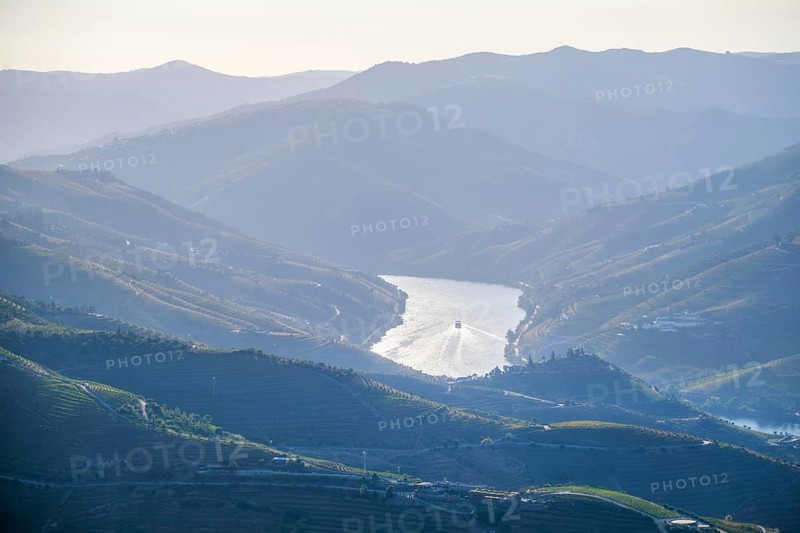Aerial drone view of a tourist boat on the Douro River surrounded by layered mountain hills and vineyards in the Douro Valley, Portugal