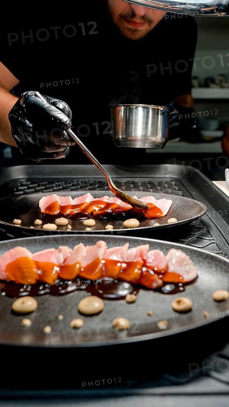 A skilled chef in a restaurant kitchen artfully applies a rich sauce to a gourmet dish. The elegant presentation of this exquisite meal exemplifies culinary artistry