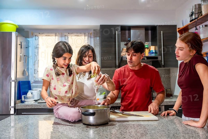 Family cooking together in a modern kitchen, parents teaching children to prepare healthy meal ingredients, bonding over teamwork, learning, and everyday home joy