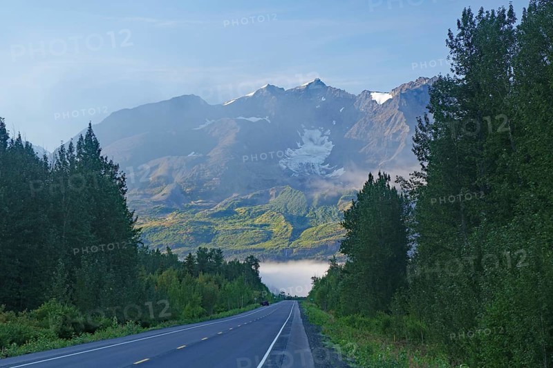 Traffic-free road leads as grades towards rugged mountains, morning fog, Richardson Highway, Alaska, USA