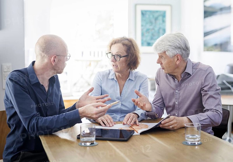 Symbolic photo on the subject of counselling. An older woman and an older man sit together at a table at home and receive counselling from a young man. Berlin, 13.08.2024