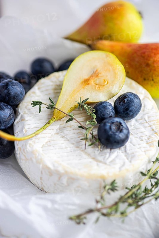 A close up image showcasing creamy Brie cheese paired with ripe, juicy pears and fresh blueberries. Fresh thyme enhances the gourmet elegance of this delightful arrangement