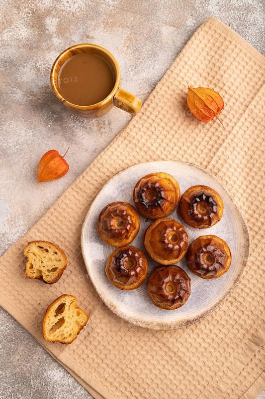 Golden caramelized Canele cookies dessert, cup of coffee, on brown concrete background with beige textile, close up, top view, flat lay