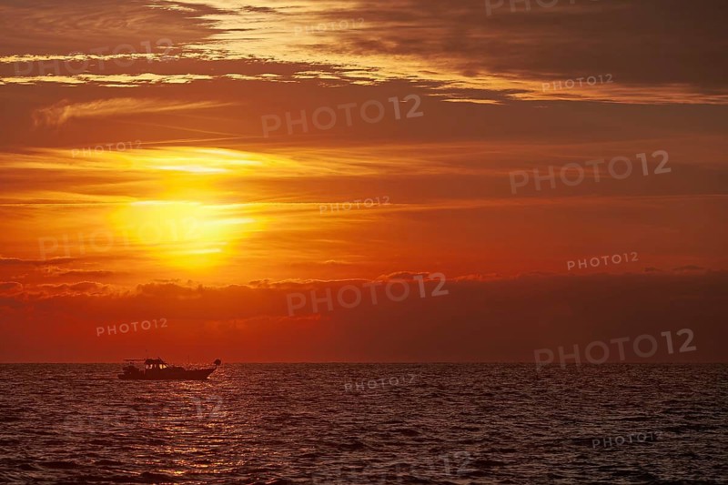 A boat sails across the sea at sunset, the sky is colored in bright orange and red, Cyprus
