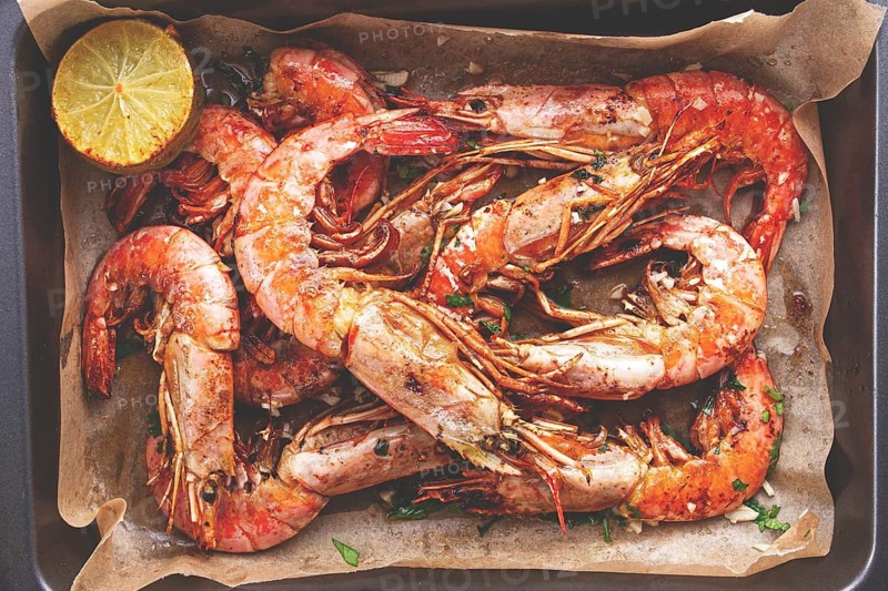 Juicy grilled shrimp, placed on a baking sheet lined with parchment paper, garnished with herbs and lemon