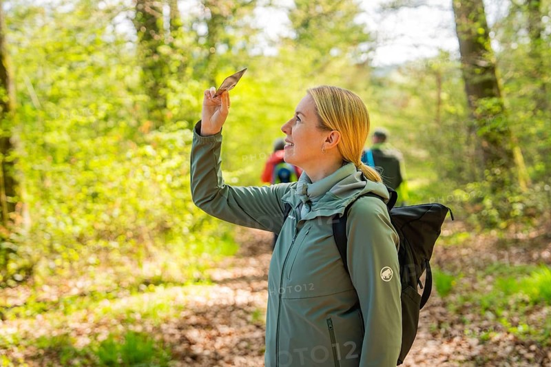 Smiling woman holding a leaf surrounded by spring-like forest landscape, Heckengäu nature tour, Aidlingen, Böblingen district, Germany