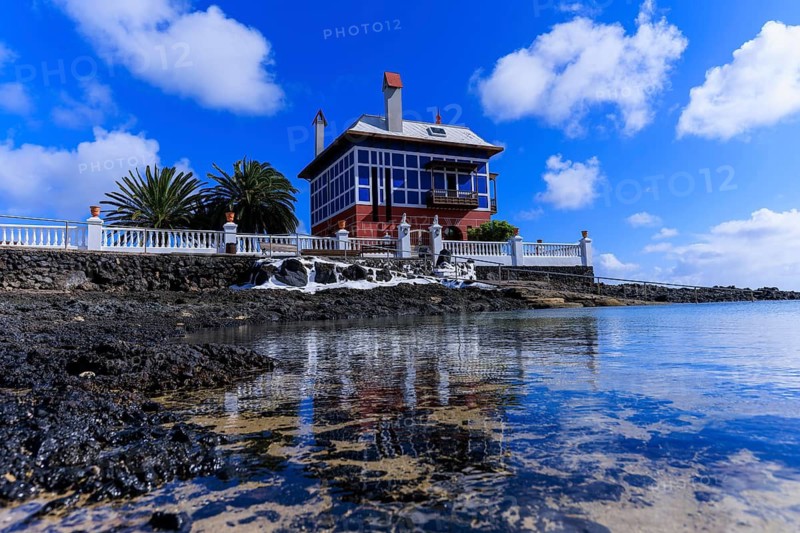 Lanzarote, Canary Islands, Spain, Europe, Arrieta Blue House, A house at the water's edge with its reflections and surrounded by palm trees under a blue sky