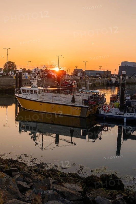 Fishing boat in harbor at sunset, calm water with reflections and calm atmosphere, Howth, Ireland