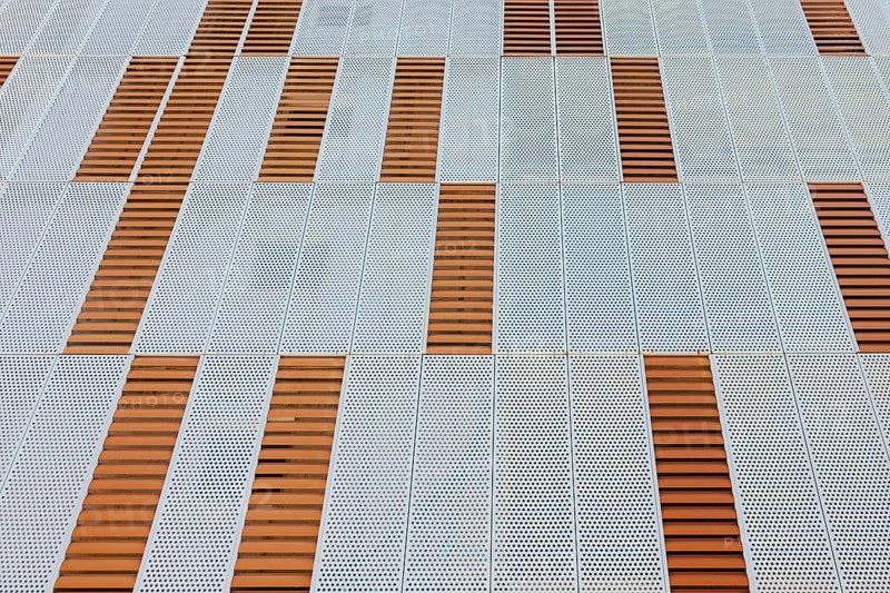 An abstract geometric pattern on a building facade showcases perforated metal panels with alternating wood sections. This urban design emphasizes modern architectural aesthetics