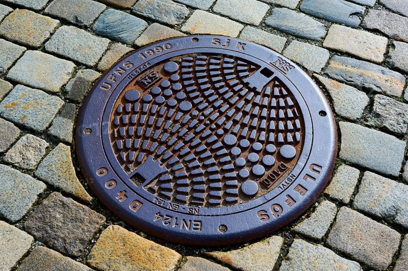 Round manhole cover with geometric pattern on cobblestones, Bergen, Vestland, Norway