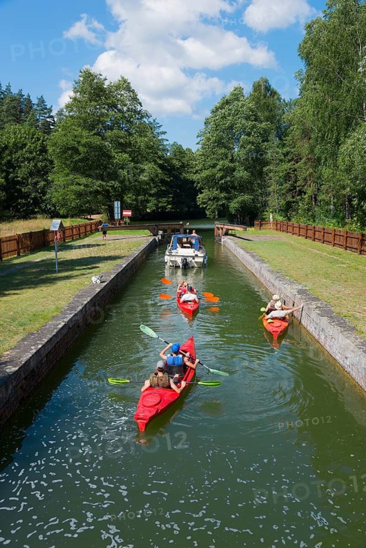 Kayakers and a boat enjoying a summer day on a narrow canal with green surroundings, Sluza Paniewo, lock between the lakes Paniewo and Krzywe, Plaska, Powiat Augustowski, Podlaskie Voivodeship, Poland