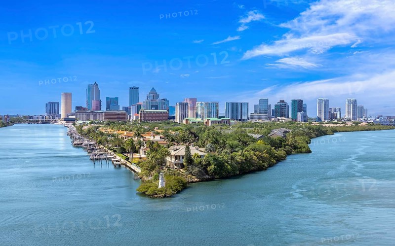 Aerial view of Tampa, Florida, featuring a lush waterfront peninsula with luxury homes, private docks, a small lighthouse, and the downtown city skyline in the background