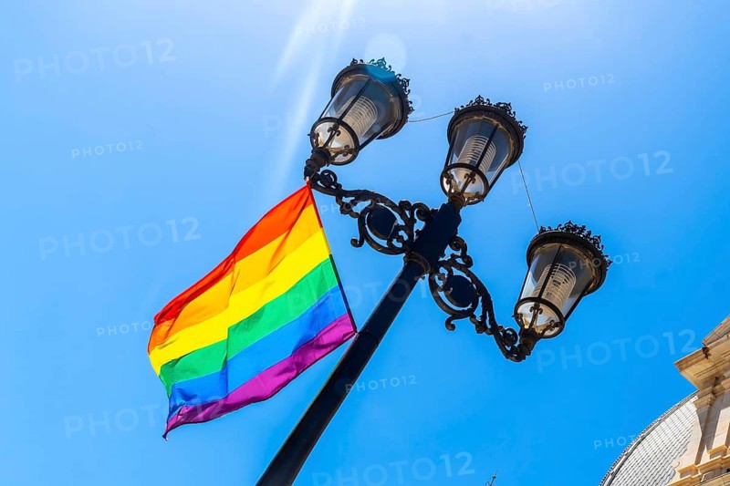 Rainbow flag displaying diverse colors proudly flying on a historic street lamp against a clear blue sky in the city of cartagena, promoting inclusion and support for lgbtq plus community